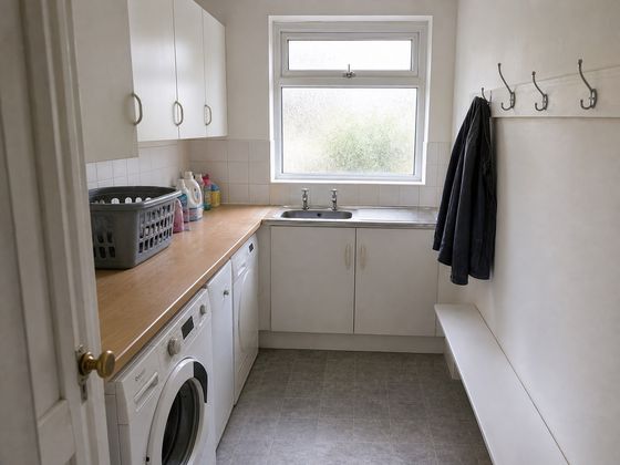 Plain compact British utility room with exposed appliances, white cupboards, old vinyl floor, sink and small window before redesign.
